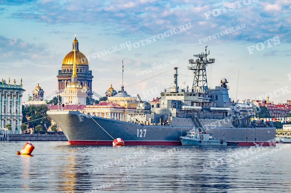 Фотография демонстрирует военный корабль на фоне исторического центра Санкт-Петербурга. Корабль, видимо, стоит на якоре на Неве, а городская архитектура в качестве фона создает контраст между современностью и историей. Такие фотографии могут использоваться в материалах, посвященных Дню ВМФ, в патриотической тематике, для образовательных статей о военно-морском флоте или как часть выставок, рассказывающих о военной истории Санкт-Петербурга.